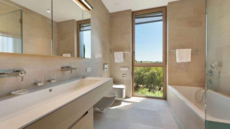 Modern bathroom with double sink, bathtub, bidet and large window with green view in design villa.