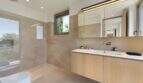 Modern bathroom with light wooden vanity, natural stone tiles and large mirror in design house S'Alqueria Blanca