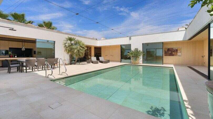 Modern courtyard pool with terrace, lounge furniture and large glass fronts in design villa S'Alqueria Blanca