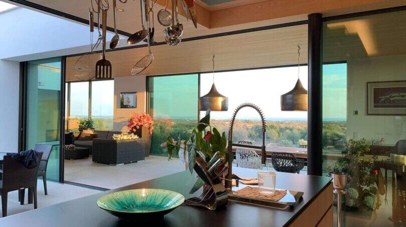 Modern design kitchen with cooking island, hanging utensils and panoramic windows with sea view in S'Alqueria Blanca
