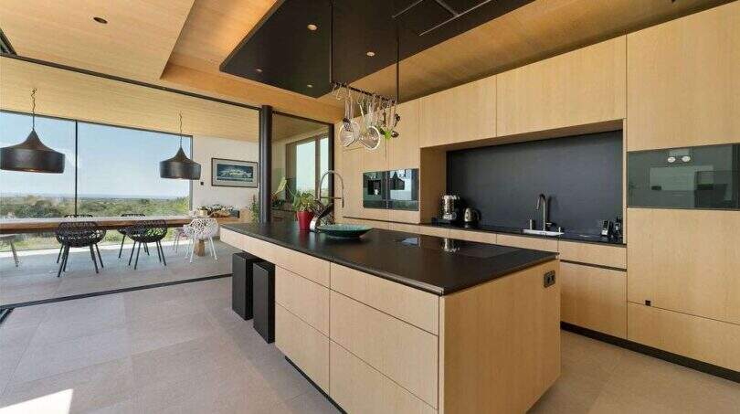 Modern design kitchen with cooking island, wooden fronts and panoramic windows with sea view in S'Alqueria Blanca