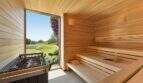 Luxury sauna with wooden cladding, sauna stove and large window with garden view in modern design house