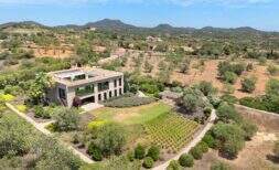 Foto aérea de casa de diseño moderno en S'Alqueria Blanca con amplio jardín, olivos y vistas panorámicas a las montañas.