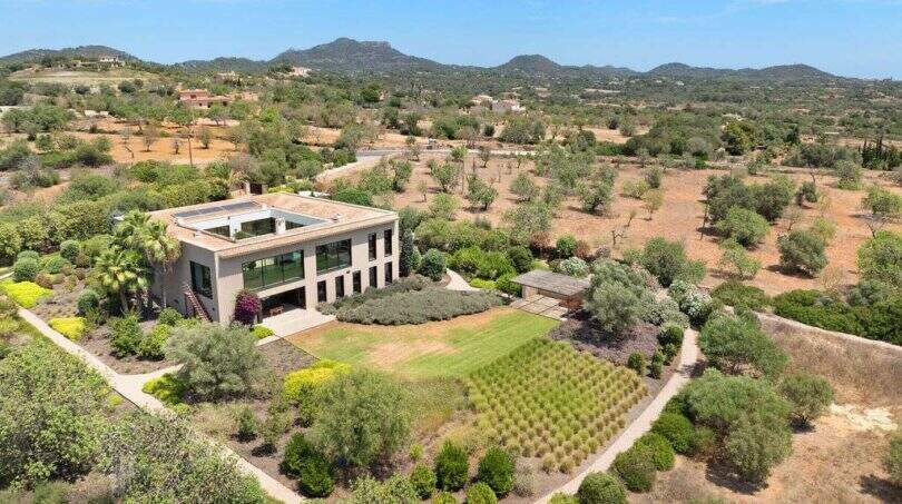 Aerial view modern design house in S'Alqueria Blanca with spacious garden, olive trees and mountain panorama.
