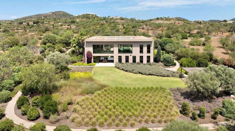 Aerial view modern design house in S'Alqueria Blanca with well-maintained garden, green spaces and hilly landscape