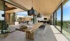 Covered terrace with rustic wooden table, designer chairs and panoramic glazing with sea view in S'Alqueria Blanca