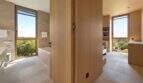 Modern bathroom with wooden elements, built-in bathtub and panoramic windows with nature view in S'Alqueria Blanca.