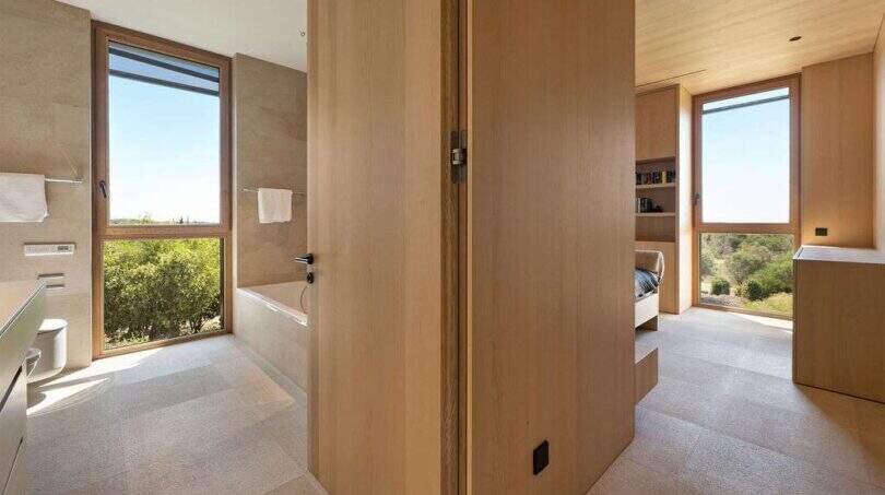 Modern bathroom with wooden elements, built-in bathtub and panoramic windows with nature view in S'Alqueria Blanca.
