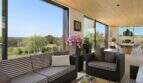 Elegant living area with panoramic windows, rattan furniture and sea view in modern design house in S'Alqueria Blanca.