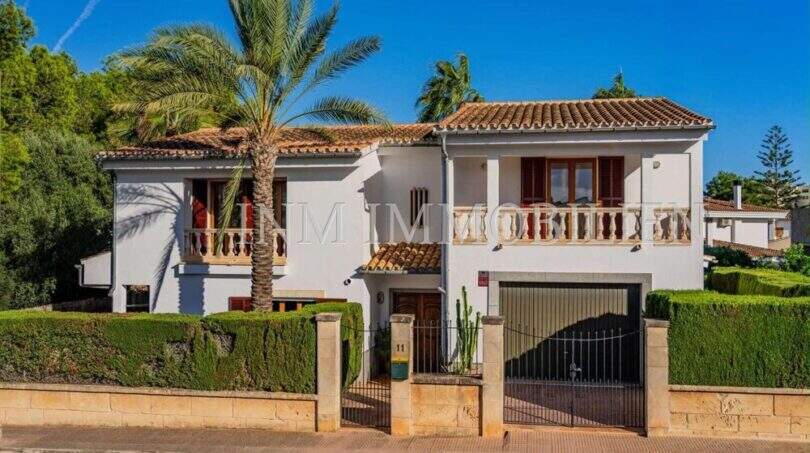 Außenansicht mediterranes Einfamilienhaus Sa Coma: weiße Fassade, Terrakottadach, Palme, Balkon, Garage und gepflegte Hecken.