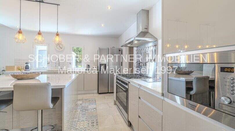 Moderne weiße Einbauküche mit Edelstahlgeräten, Kochinsel und Pendelleuchten in mediterraner Villa Sa Coma