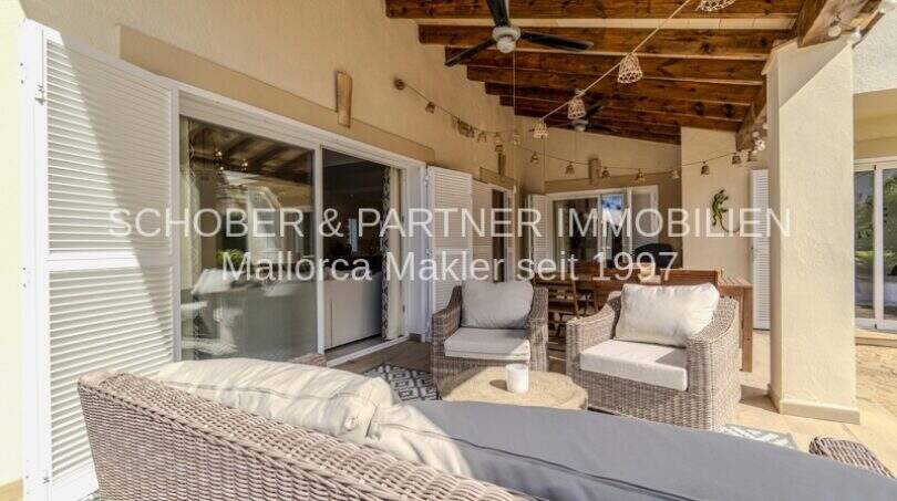 Überdachte Terrasse mit Rattanmöbeln, Holzbalkendecke und Deckenventilator einer mediterranen Villa in Sa Coma.