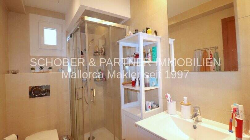 Baño luminoso con ducha de cristal, lavabo y estantería blanca en cuidado apartamento de 4 habitaciones en Porto Cristo
