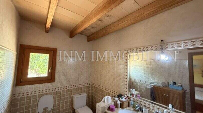 Rustikales Badezimmer der Finca Llucmajor mit Holzbalkendecke, Mosaikfliesen, Waschbecken und WC.