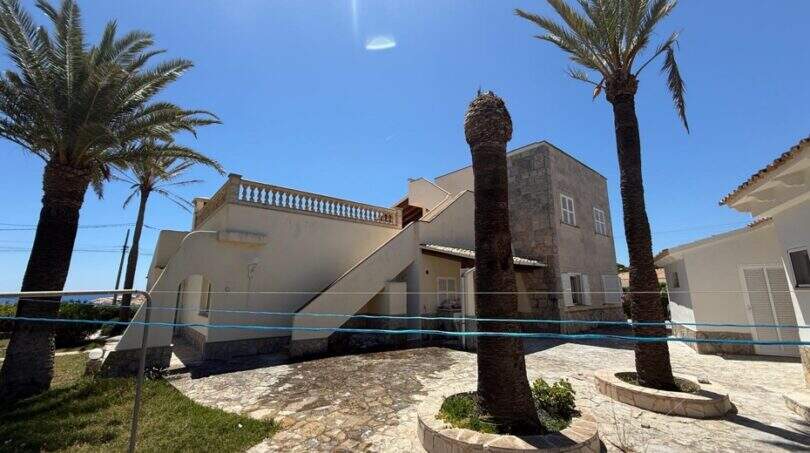 Außenansicht mediterrane Villa in Cala Murada mit Palmen, Steinterrasse und Außentreppe unter blauem Himmel.