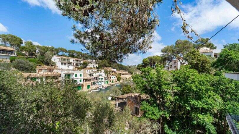 Blick auf den malerischen Hafen von Cala Figuera mit weißen Häusern, üppiger Vegetation und türkisblauem Wasser