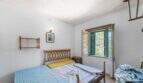 Helles Schlafzimmer der Villa in Cala Figuera mit Holzbetten, grünen Fensterläden und Blick ins Grüne.