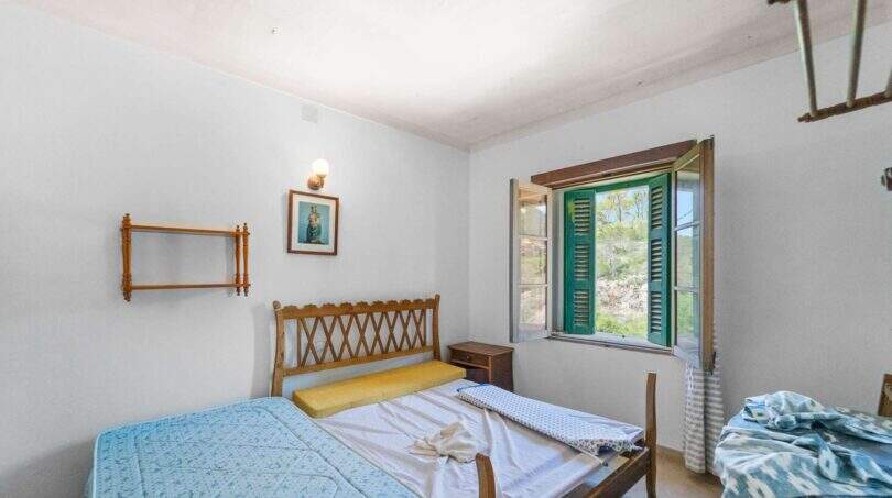 Helles Schlafzimmer der Villa in Cala Figuera mit Holzbetten, grünen Fensterläden und Blick ins Grüne.