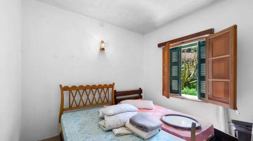 Helles Schlafzimmer der Villa Cala Figuera mit Doppelbett, Holzkopfteil und Fensterläden mit Gartenblick.