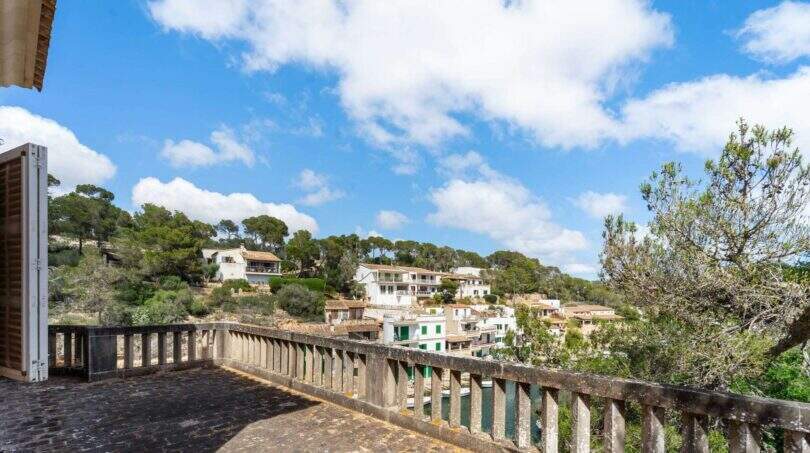 Steintetrasse mit Balustrade und Panoramablick auf Cala Figuera, weiße Häuser am Hang, Pinien und blauer Himmel