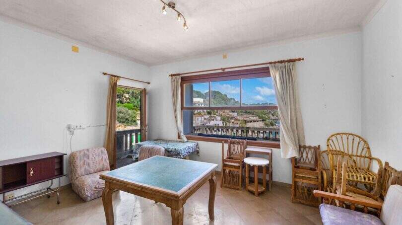 Helles Wohnzimmer der Villa in Cala Figuera mit Rattanmöbeln, Holztisch und großem Fenster mit Ortsblick.