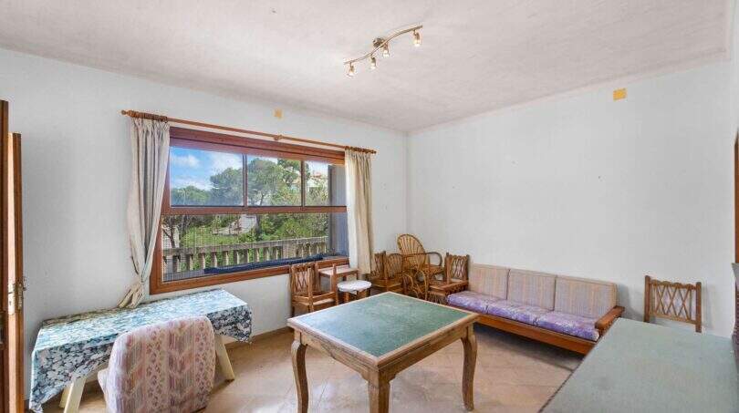 Helles Wohnzimmer der Villa in Cala Figuera mit Holztisch, Sofa und großem Fenster mit Gartenblick.