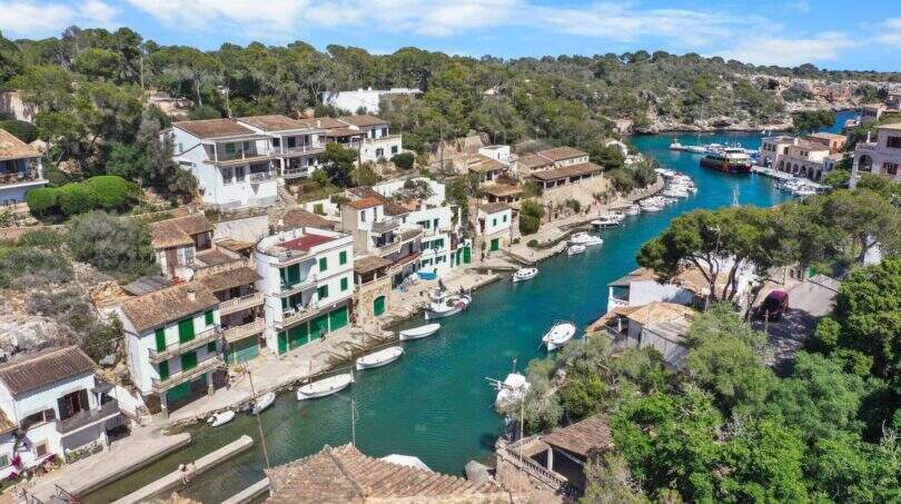 Luftaufnahme des malerischen Hafens von Cala Figuera mit türkisem Wasser, weißen Villen und Booten in erster Meereslinie.