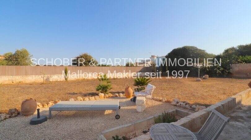 Naturnaher Garten mit Kiesbelag, Sonnenliege und mediterranen Keramiktöpfen eines sanierten Landhauses in Portocristo.