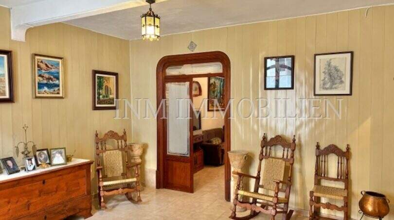 Wohnzimmer mit Holzvertäfelung, zwei Schaukelstühlen, Pendelleuchte und elegantem Holzdurchgang zum Nachbarzimmer.