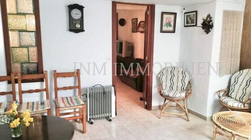 Wohnzimmer mit Korbmöbeln, Holzstühlen, Wanduhr und Durchgang zum Nebenraum im Dorfhaus Felanitx