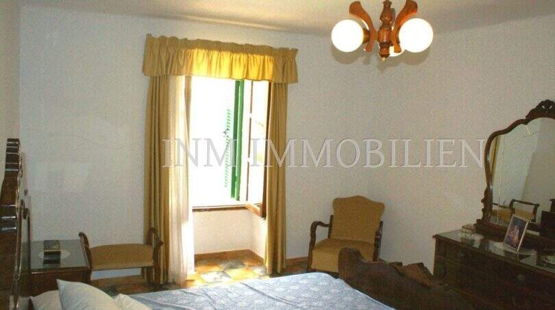 Schlafzimmer mit Doppelbett, goldfarbenen Vorhängen, Holzmöbeln und Fenster zum Patio im Dorfhaus Felanitx