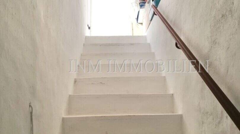 Enge weiße Kellertreppe mit Holzhandlauf im Dorfhaus Felanitx, führt zu Abstellraum mit Holzbalkendecke