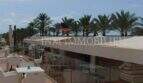 Sonnenterrasse der Bar/Cafeteria an der Playa de Palma mit weißen Möbeln, Glasgeländer und Palmenblick.