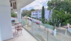Moderner Balkon mit Glasgeländer und Gartenmöbeln, Blick auf Straße und weiße Apartments in Palmanova