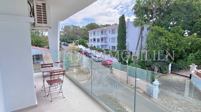 Moderner Balkon mit Glasgeländer und Gartenmöbeln, Blick auf Straße und weiße Apartments in Palmanova