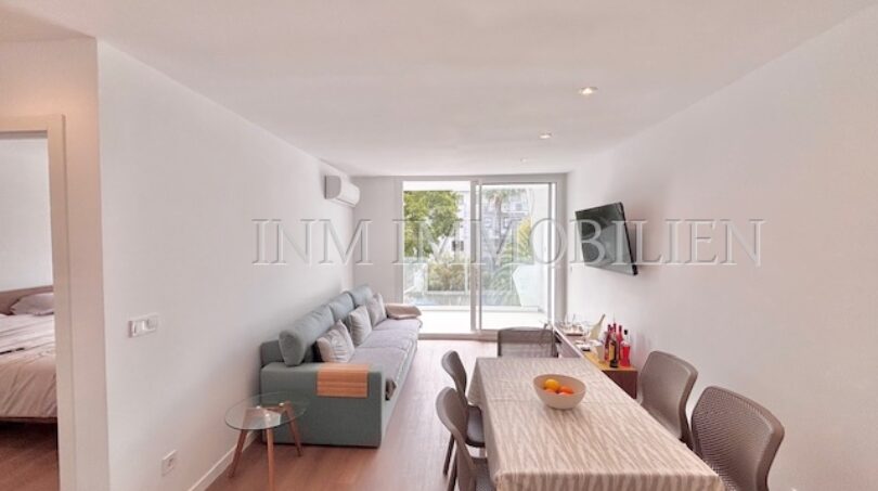 Helles Wohnzimmer mit grauem Sofa, Esstisch und Balkon in renoviertem Apartment Palmanova