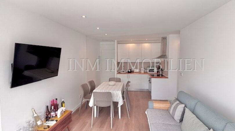 Helles Wohnzimmer mit Sofa, Esstisch und offener Küche in renoviertem Apartment in Palmanova