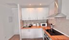 Moderne weiße Einbauküche mit Holzarbeitsplatte, Induktionsherd, Dunstabzug und Mikrowelle im Apartment Palmanova