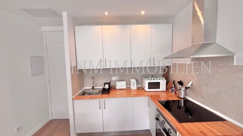 Moderne weiße Einbauküche mit Holzarbeitsplatte, Induktionsherd, Dunstabzug und Mikrowelle im Apartment Palmanova