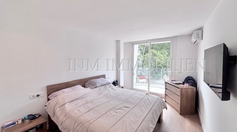 Helles Schlafzimmer mit Doppelbett, Holzmöbeln, Wand-TV und Zugang zur Terrasse in Palmanova-Apartment