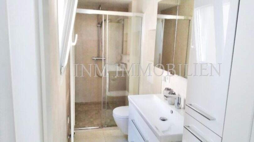 Modernes Badezimmer im Penthouse Playa de Palma mit Glasdusche, weißem Waschtisch und Spiegelschrank.
