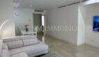Helles Wohnzimmer mit grauem Ecksofa, Marmorboden, TV-Wand und Essbereich in moderner Luxuswohnung in Bendinat.