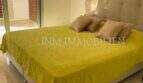 Helles Schlafzimmer mit Doppelbett, gelbem Überwurf und Zugang zur Terrasse in Luxuswohnung Bendinat