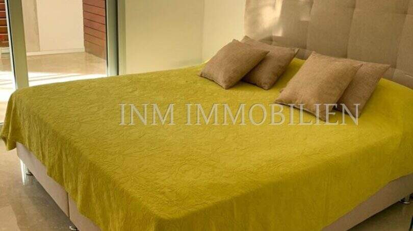 Helles Schlafzimmer mit Doppelbett, gelbem Überwurf und Zugang zur Terrasse in Luxuswohnung Bendinat