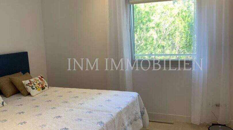 Helles Schlafzimmer der Luxuswohnung in Bendinat mit Doppelbett, Marmorboden und Fenster mit Grünblick.