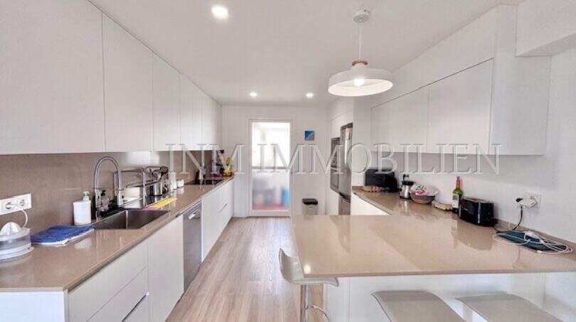 Moderne weiße Küche mit Kochinsel, Barstühlen und Holzboden in möblierter Wohnung in Can Pastilla, Palma.