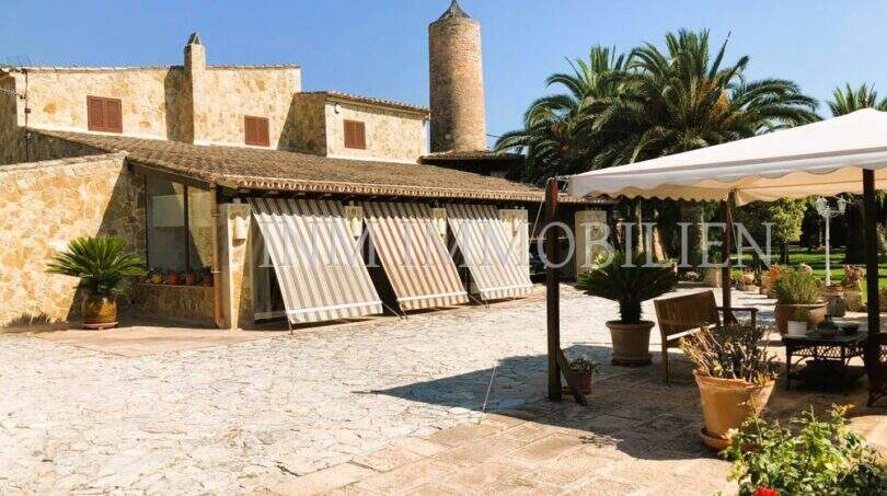 Rustikaler Innenhof mit Natursteinpflaster, Palmen, Windmühle und überdachter Terrasse in S'Aranjassa, Palma