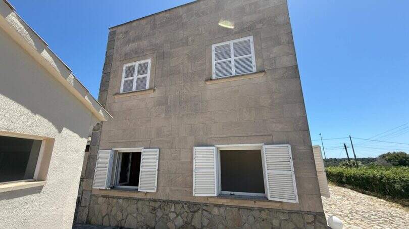 Zweistöckige Steinvilla in Cala Murada mit weißen Fensterläden, gepflastertem Innenhof und mediterranem Charakter.