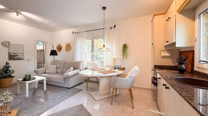Helles Wohn-Esszimmer mit offener Küche, weißem Esstisch und grauem Sofa in der Strandwohnung Cala Murada