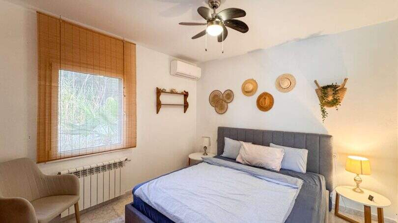 Helles Schlafzimmer mit Doppelbett, Klimaanlage, Deckenventilator und dekorativen Strohhüten in Cala Murada.